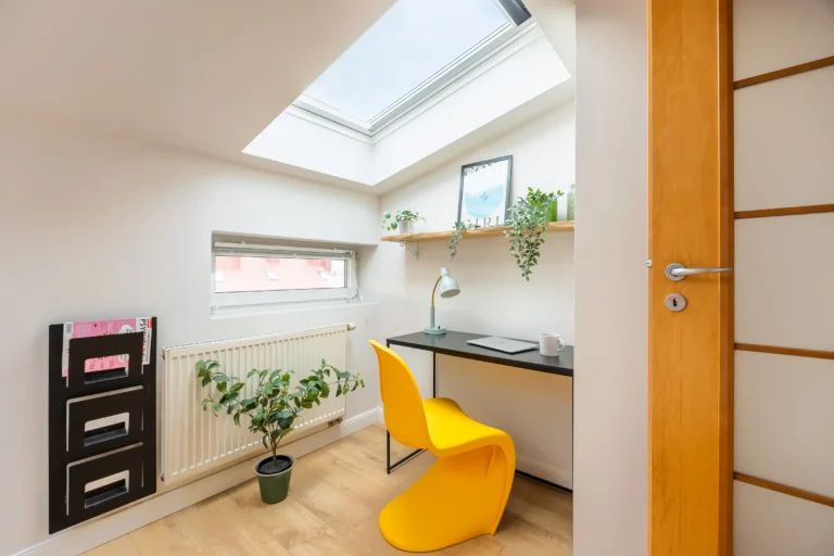 Małe biurko i żółte krzesło w pokoju z oknem dachowym.