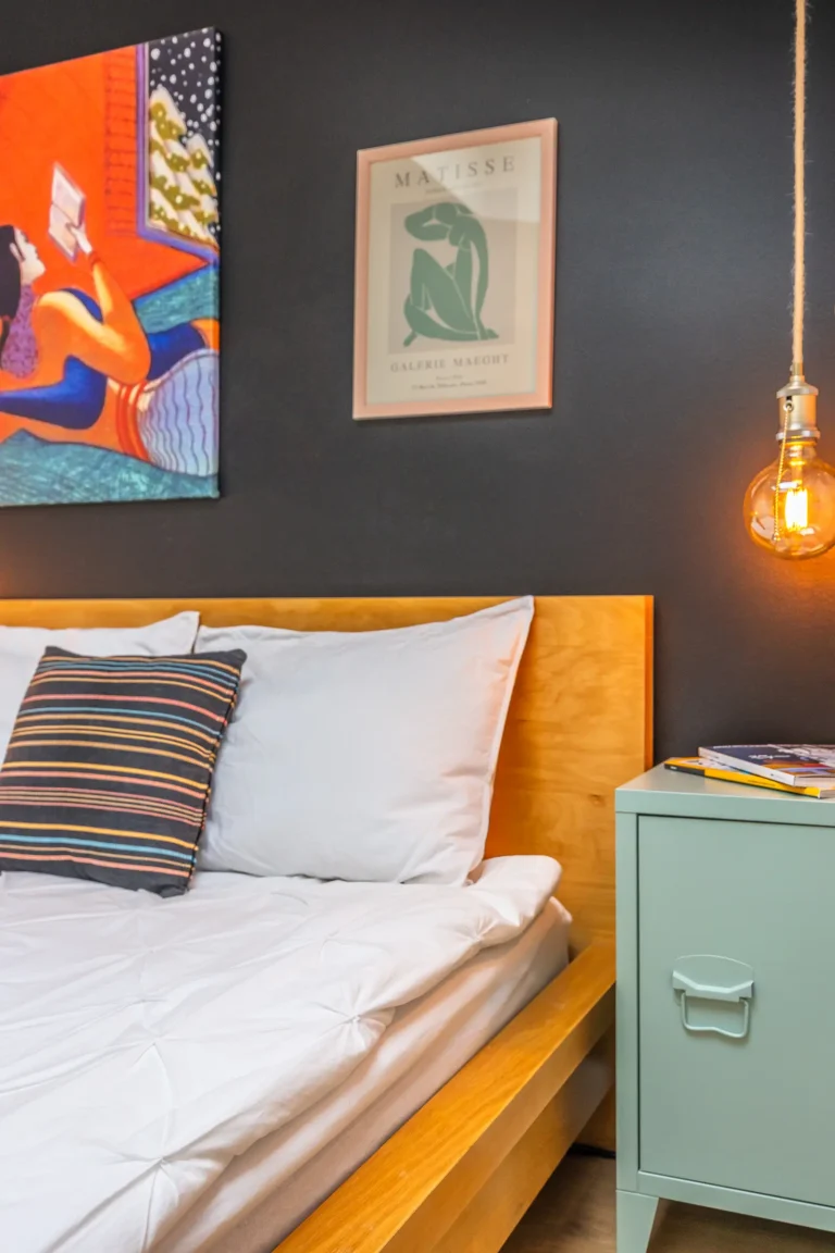 Ciepłe światło żarówki oświetla łóżko i szafkę nocną.