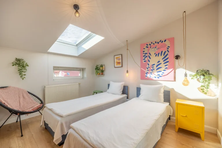 Słoneczna sypialnia na poddaszu z dwoma łóżkami i żółtą szafką nocną.