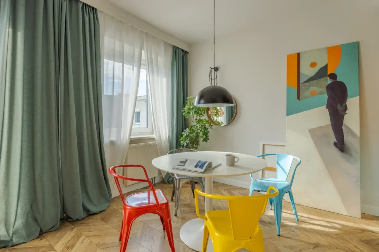 Jadalnia z okrągłym stolem, kolorowymi krzesłami i dużym kolorowym obrazem.