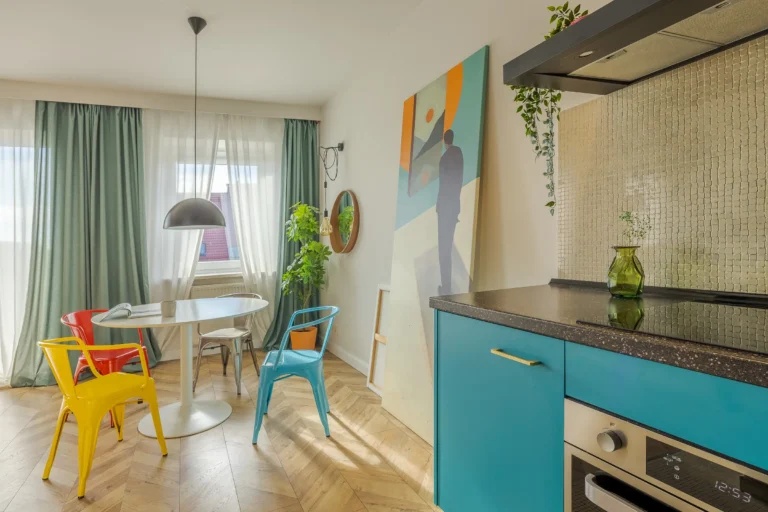 Jadalnia z okrągłym stołem i kolorowymi krzesłami obok kuchni z niebieskimi szafkami.