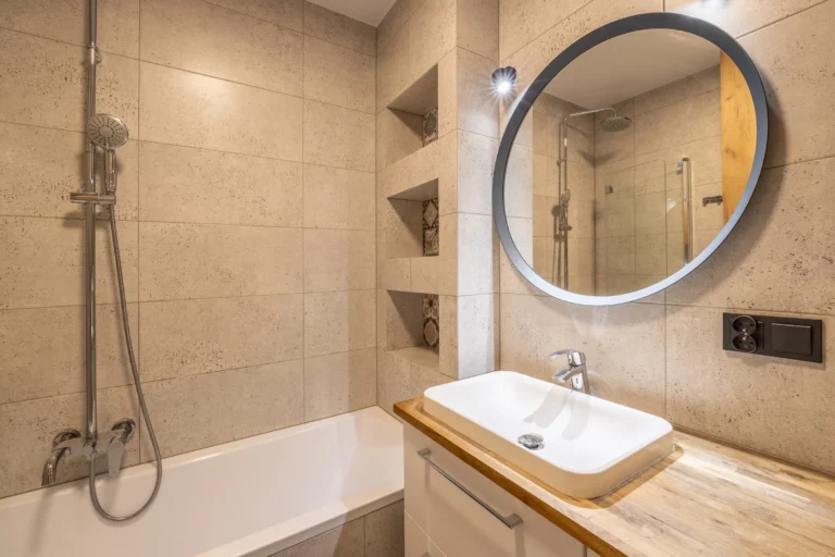 Jasna łazienka z okrągłym lustrem i beżowymi płytkami.