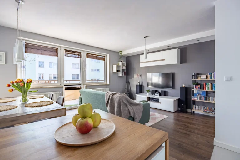 Salon mieszkania w bloku z drewnianym stołem jadalnianym i zieloną kanapą.