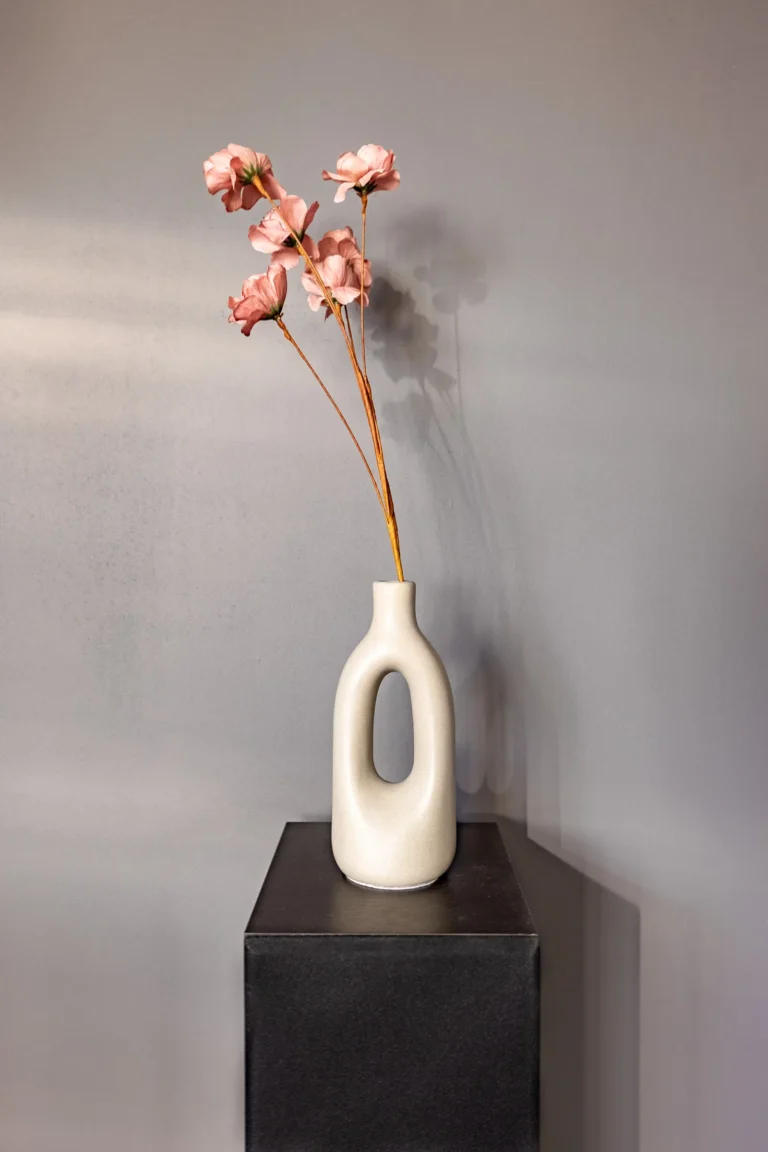 Różowe suche kwiaty w beżowym wazonie rzucają cień na ścianę.